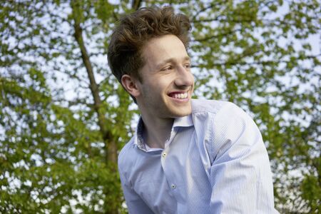 Portrait of a young handsome happily laughing man looking over his shoulder in beautiful greeneryの写真素材