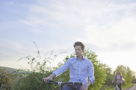 Young couple riding bicycle in greenery, young man in the foreground young woman in the backgroundの写真素材