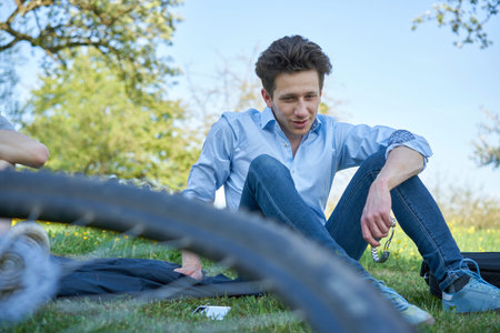 Young talking man sitting in a lawn during a bike tour in beautiful greeneryの写真素材