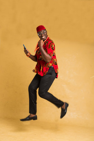 Igbo Traditionally Dressed Business Man in Mid Air with Phone in Hand Side Viewの写真素材
