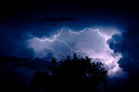 Night sky with lightning during a thunderstorm. Dramatic weather. Big clouds, light electric effects.の写真素材