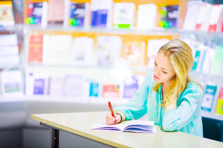 Young girl doing homework on a library background