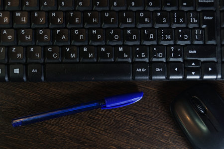 Black keyboard and mouse with blue ballpoint pen lying on dark tableの写真素材