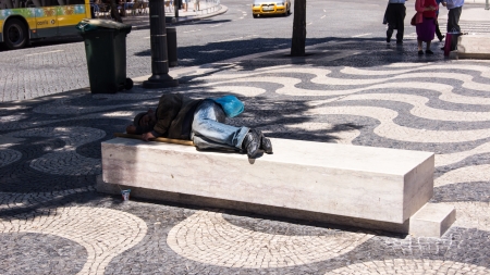 A homeless man on the Rossio Square, in the shadow on a bench in Lisbon, Portugal  Lisbon has a lot of homeless people but fed and clothed by the state のeditorial素材