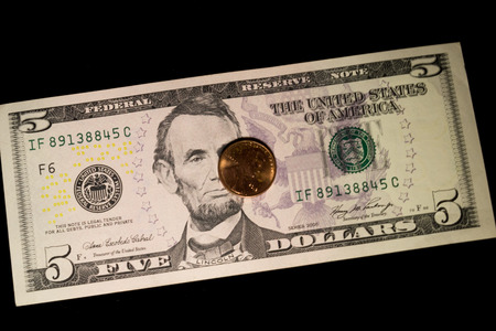 A US five dollar bill and coin on a black background の写真素材