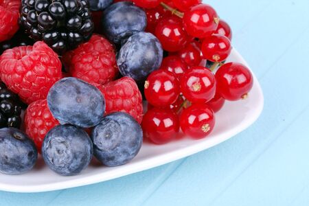 Different berries on white plate, closeup on blue backgroundの写真素材