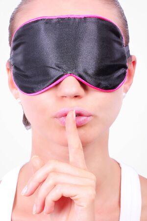 Woman in sleeping mask making a keep it quiet gesture, closeup on white backgroundの写真素材