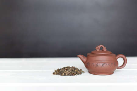 Chinese teapot and pile of green tea on white tableの写真素材