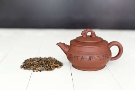 Chinese teapot and pile of green tea on white tableの写真素材
