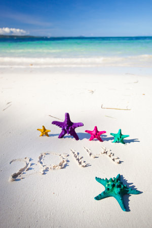 Numbers 2014 on white sandy beach with color starfishesの写真素材