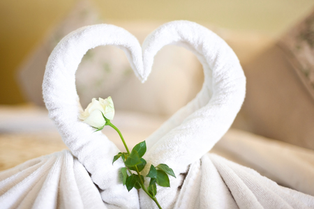 Two white towels swans on bed sheet, decorated rose and heart in hotel roomの写真素材