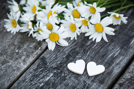 Bouquet of fresh camomiles with wooden hearts on old wooden table. Valentine's holiday romantic card concept.の写真素材