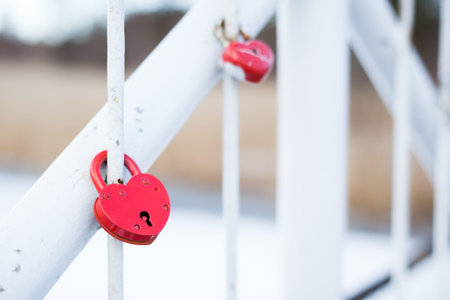 Red heart-shaped locks locked on fence of the white bridgeの写真素材