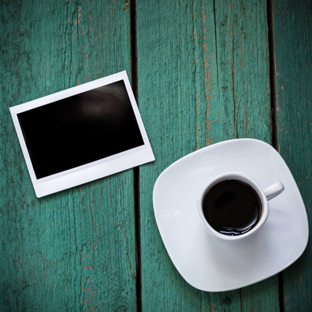Empty photo card and a cup of coffee on old green wooden board, memory concept