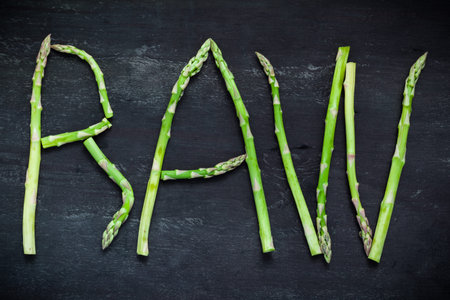 Word Raw made of asparagus vegetables on black wooden board, top view.  Healthy food concept.の写真素材