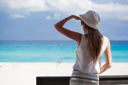Woman in summer hat on balcony looking to the turquoise sea and white perfect sandy beach, enjoying life and summer vacation, rear viewの写真素材