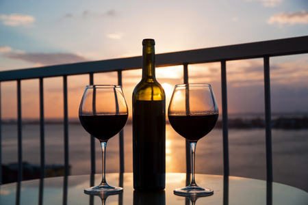 Silhouette of bottle and glasses with red wine in sunset with sea view backgroundの写真素材