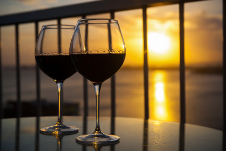 Two red wine glasses in front of the setting sun. Balcony view with Caribbean sea backgroundの写真素材