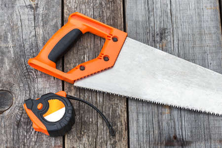 Handsaw and  measuring tape on a wooden board, closeupの写真素材
