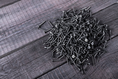 Pile of black screws closeup on wooden background
