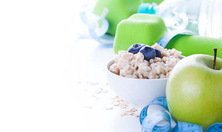 Fitness frame with energy breakfast, oatmeal, apple and mineral water with sport tools on background. Healthy lifestyle concept with copy space.の写真素材