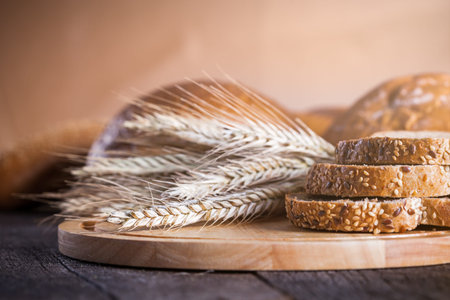 Different fresh baked breads on board with golden wheat ears on wooden rustic table