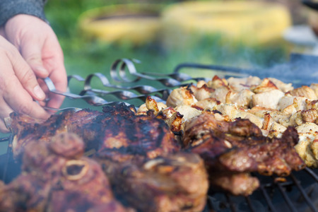 Cooking lamb steaks and pork kebab on grill, skewered pork meat in hand, outdoor. Selective focus and shallow DOFの写真素材