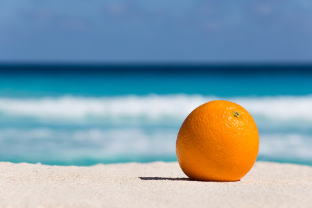 Orange fruit on sand against turquoise caribbean sea water. Tropical summer vacation conceptの写真素材