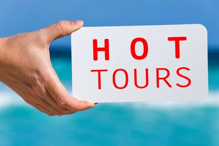 White board with sign Hot Tours in female hand  against turquoise caribbean sea water. Tropical summer vacation conceptの写真素材