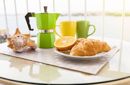 Delicious breakfast with coffee on hotel's balcony, fresh croissants and slice of orange fruit with coffee percolator backgroundの写真素材