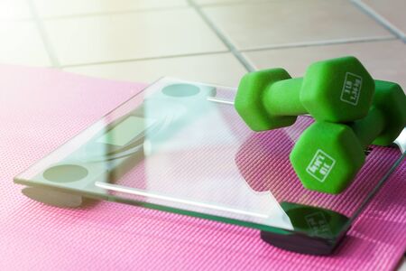 Green dumbbels on  digital glass fitness scales with pink yoga mat, Shallow DOF. Weight loss sport conceptの写真素材