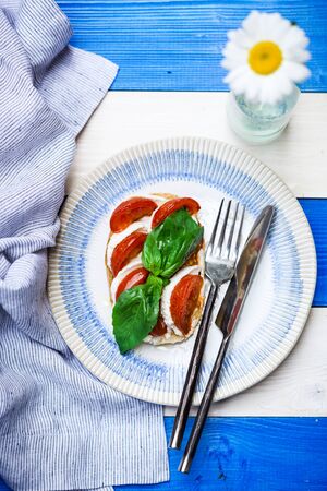 Bruschetta with cherry tomato, mozzarella and basil leaves on color aquatic style wooden background, decorated camomile flowerの写真素材