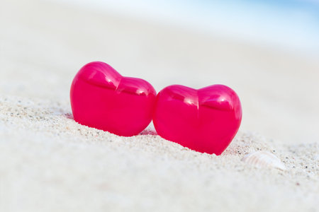 Red decoration hearts on sandy beach with sea background,  shallow depth. Valentines day card and love to travel conceptの写真素材