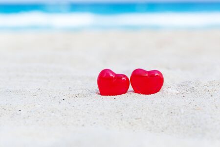 Red decoration hearts on sandy beach with sea background,  shallow depth. Valentines day card and love to travel conceptの写真素材