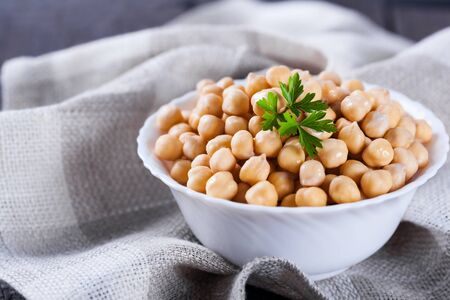 Gold chick peas in bowl with parsley leaves decorated tablecloth on wooden background, healthy vegetarian bean food with a lot of proteinの写真素材