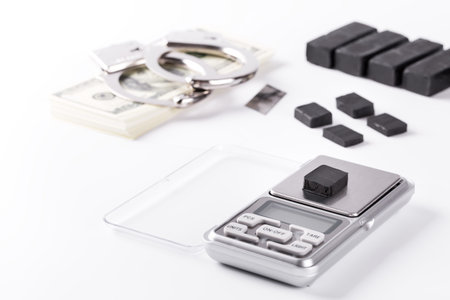 Blocks of hashish on digital scales over white background. Drug dealer is arrested in process of weighing hash for illicit dealの写真素材