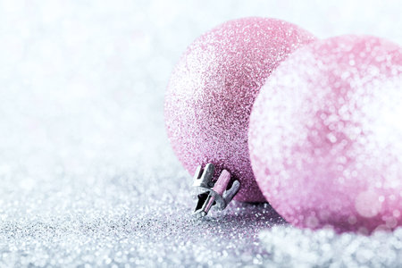 Pink Christmas baubles on silver glitter with defocused lights on background, New Year greeting card. Shallow depth of field.の写真素材