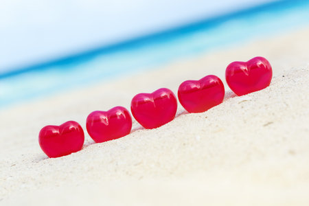Red decoration hearts on sandy beach with sea background,  shallow depth. Valentines day card and...