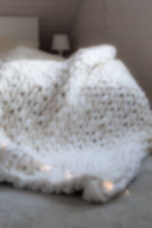 Cozy white scandinavian bedroom interior. Beautiful merino woolen plaid decorated bed and floor, super chunky yarn knitted blanket, out of focus, blurred styleの写真素材