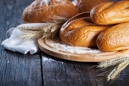 Fresh bakery goods. Different types of bread with sheaves of golden wheat on rustic wooden board.