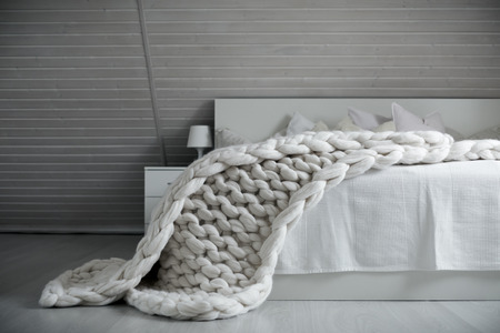 Cozy white scandinavian bedroom interior. Beautiful merino woolen plaid decorated bed and floor, super chunky yarn knitted blanket, nobodyの写真素材