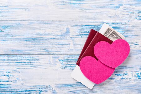 Heart shapes on passports with boarding pass and dollar banknotes on blue rustic wooden backgroundの写真素材