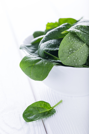 Fresh raw organic baby spinach in bowl on white wooden board, diet conceptの写真素材
