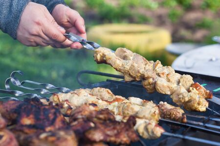Cooking lamb steaks and pork kebab on grill, skewered pork meat in hand, outdoor. Selective focus and shallow DOFの写真素材