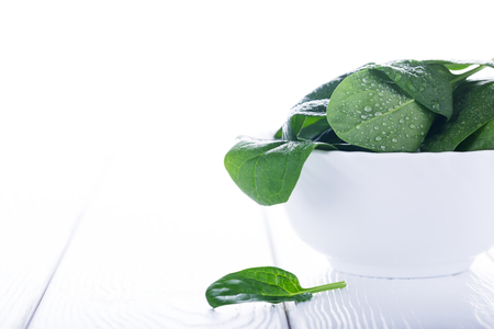 Fresh raw organic baby spinach in bowl on white wooden board, diet conceptの写真素材