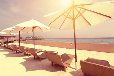 White parasol with sun chairs against sunlight, perfect summer vacation on Maldives island, warm toned image.の写真素材
