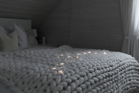 Cozy white scandinavian bedroom interior at evening time. Beautiful merino woolen plaid decorated...