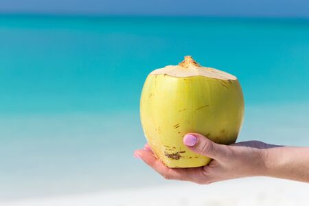 Fresh coconut cocktail in hand on turquoise sea background, travel cardの写真素材
