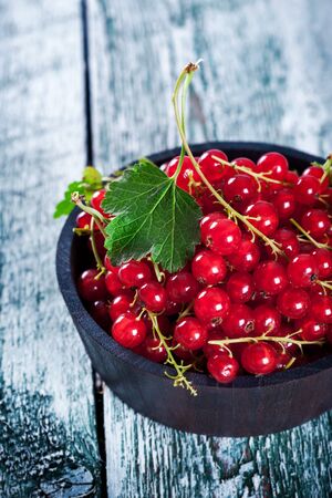 Ripe red currant in wooden bowl on wooden rustic tableの写真素材