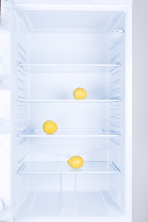 Lemon fruits on glass shelf in empty clean refrigerator, nobody. Using citrus for fresh smell inside.の写真素材